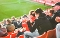 Zuschauer in Winterkleidung sitzen auf roten Sitzen in einem Stadion und schauen auf das Spielfeld