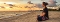 Frau sitzt im Schneidersitz am Strand und blickt auf das Meer bei Sonnenuntergang