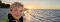 Frau mit kurzem blondem Haar und schwarzem Schal am Strand bei Sonnenuntergang
