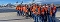 Gruppe von Personen in orangen Warnwesten steht auf einem Flughafen vor zwei Flugzeugen.