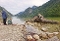 Zwei Kinder am Ufer eines Bergsees mit klarem Wasser und einem großen Treibholzstück im Vordergrund