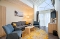 Suite:Wohnzimmer mit grauem Sofa, zwei blauen Sesseln, hellem Holztisch auf rundem gelb-grau gemustertem Teppich, Stehlampe und großem Fenster mit Vorhängen