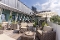 Terrasse mit Rattanmöbeln, Sitzkissen, Sonnenschirm und Pflanzen vor einem modernen Gebäude mit großen Fenstern