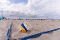 Volleyball auf Sandstrand vor Volleyballnetz mit Menschen und Strandkörben im Hintergrund unter bewölktem Himmel