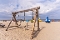 Holzschaukel mit zwei Ketten und Sitzen auf einem Sandstrand mit Strandliegen und Menschen im Hintergrund