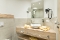 Badezimmer mit rundem Waschbecken auf Holzablage, zwei gefalteten Handtüchern, Wandspiegel, Wandföhn und Seifenspender