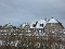 Reetgedeckte Häuser mit Schnee auf den Dächern und kahlen Hecken im Vordergrund unter bewölktem Himmel