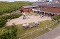 Spielplatz mit Sandfläche, Holzspielgeräten und Bänken vor einem roten Backsteingebäude in einer grünen Umgebung