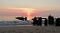 Sonnenuntergang über dem Meer mit Wellen und einer Buhne aus Holzpfählen am Strand