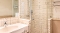 Badezimmer mit Waschbecken, Spiegel, Badewanne und Duschkabine mit Glaswand und weißen Kacheln an den Wänden