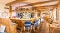 Innenraum einer Bar mit Holztheke, blauen Barhockern, maritimen Dekorationen und Tischen mit Stühlen in einem hellen Raum