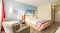 Hotelzimmer mit Doppelbett, zwei Sesseln um einen kleinen runden Tisch, blauer Wand mit Bild und Holzboden