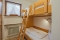 Kinderzimmer mit einem Etagenbett aus hellem Holz, Leiter, Fenster mit Gardine und Heizkörper darunter