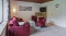 Wohnzimmer mit rotem Sofa, zwei roten Sesseln, kleinem Couchtisch, Teppich, Wandbild, Wandlampe und an der Wand montiertem Fernseher