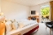 Hotelzimmer mit Doppellbett, Schreibtisch mit Stuhl, Wandfernseher und Zugang zu einem Balkon mit Sitzmöbeln
