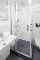 Kleine moderne Dusche mit Glasabtrennung, Handbrause, weißem Waschbecken mit Handtuch und WC in einem hellen Badezimmer