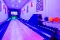 Blick auf eine Bowlingbahn mit leuchtenden Pins, bunten Bowlingkugeln auf der Ablage und abstrakten Bildern an den Wänden.