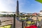 Terrasse mit Tisch, Stühlen und grünen Sitzkissen vor einem hohen Leuchtturm unter blauem Himmel