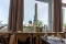 Blick aus einem Restaurantfenster auf einen hohen Leuchtturm und Häuser im Hintergrund, im Vordergrund Tische mit Stühlen und Tischdekoration
