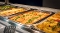 Drei große Backbleche mit paniertem Fischfilet, Zitronenscheiben und Kartoffelspalten auf einem Buffet