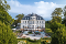 Großes historisches Herrenhaus mit Mansarddach, Terrasse mit Sonnenschirmen und gepflegtem Garten im Sommer