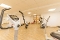 Fitnessraum mit mehreren Trainingsgeräten, darunter Ergometer, Rudergerät und Schrägbank, vor heller Holzboden- und Wandgestaltung