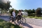 Zwei Frauen mit Fahrrädern stehen auf einem Weg neben einem Teich mit Springbrunnen im Park