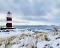 Leuchtturm mit roten und weißen Streifen an verschneitem Küstenabschnitt mit Gras und Meer im Hintergrund